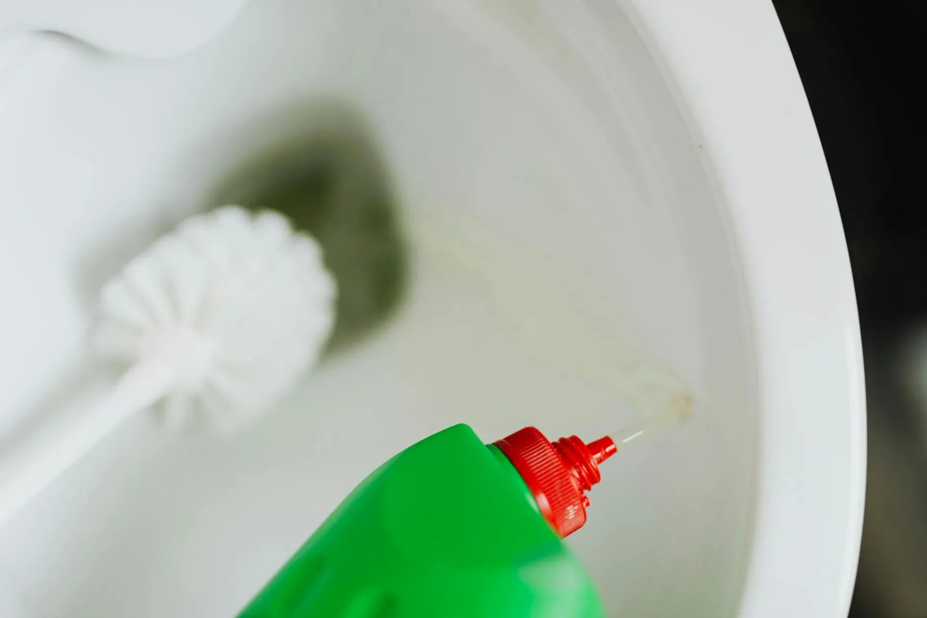 En grøn flaske med rengøringsmiddel hældes i toiletkummen for at sikre optimal hygiejne på badeværelset.