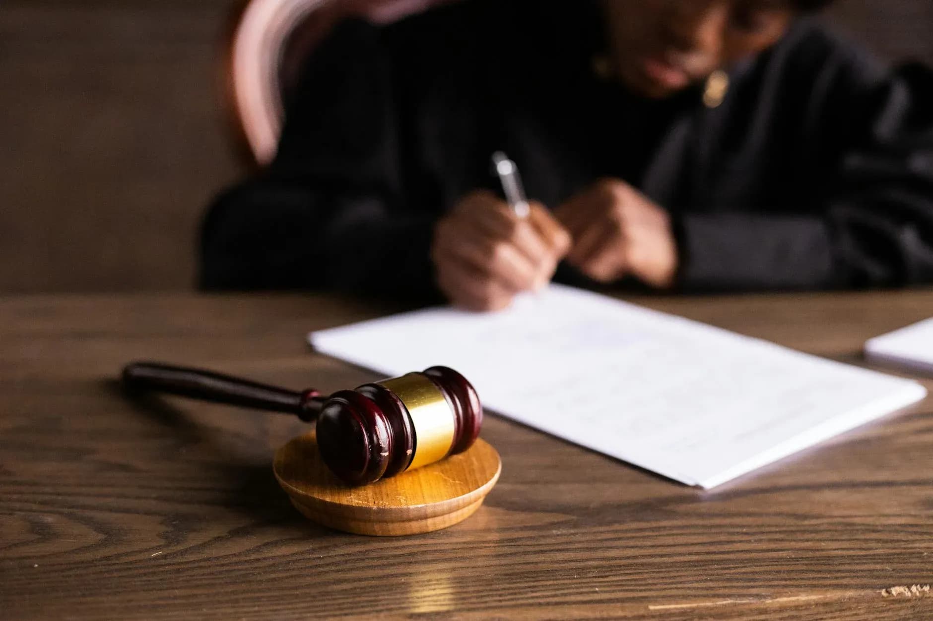 A focused shot of a judge signing documents, with the gavel symbolizing law and justice in a courtroom setting.