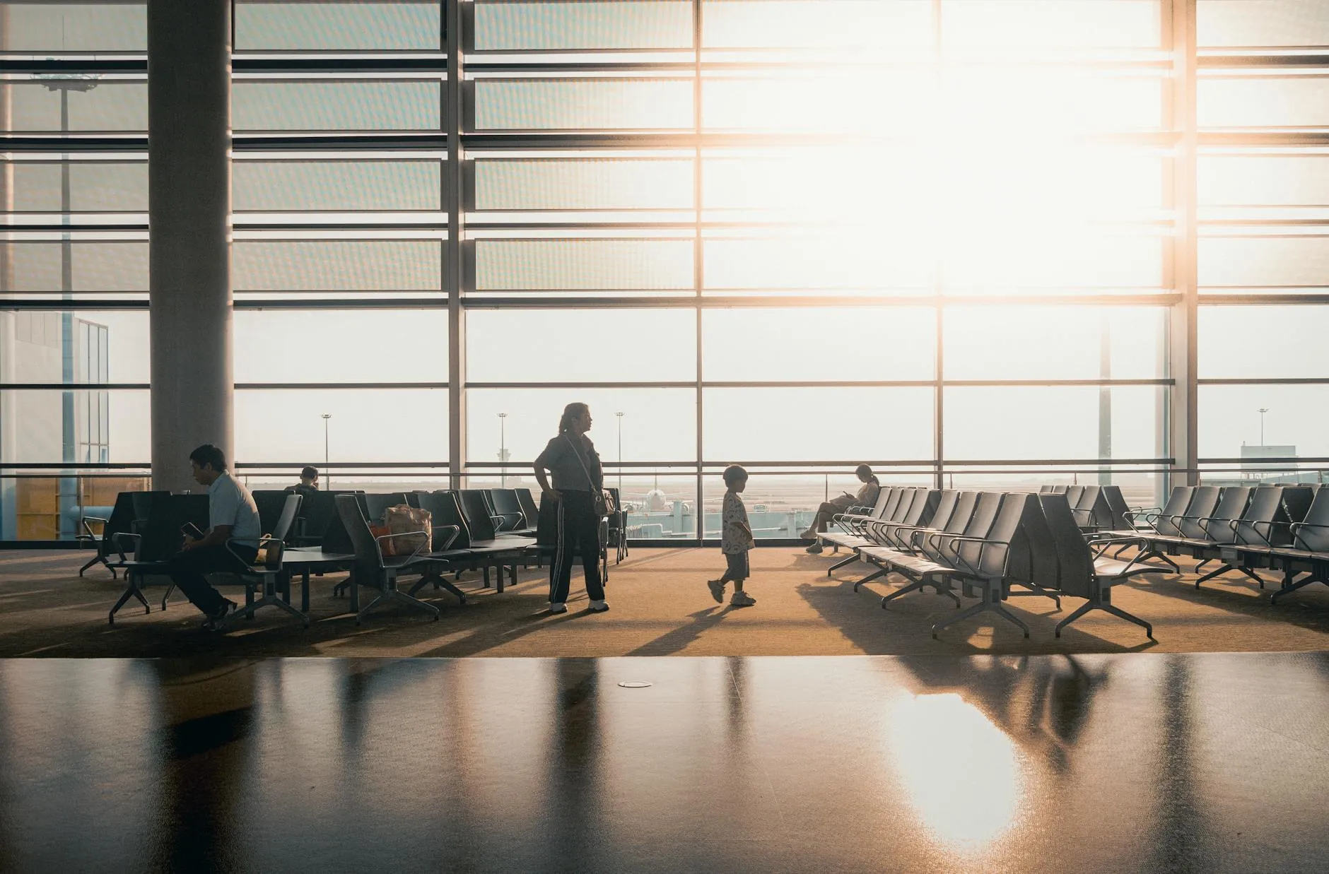 Silhuetter af rejsende bevæger sig gennem en moderne og solbeskinnet terminal i Shanghais lufthavn.