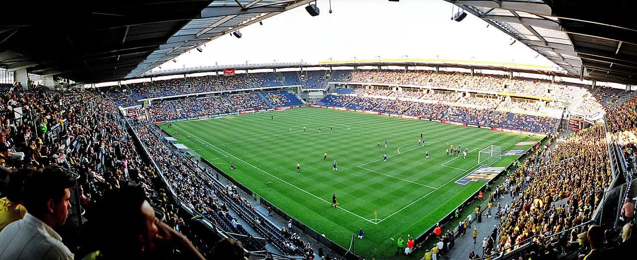 Panoramisk udsigt over Brøndby Stadion under en fodboldkamp. Billedet viser stemningen og stadionets opbygning under kamp.