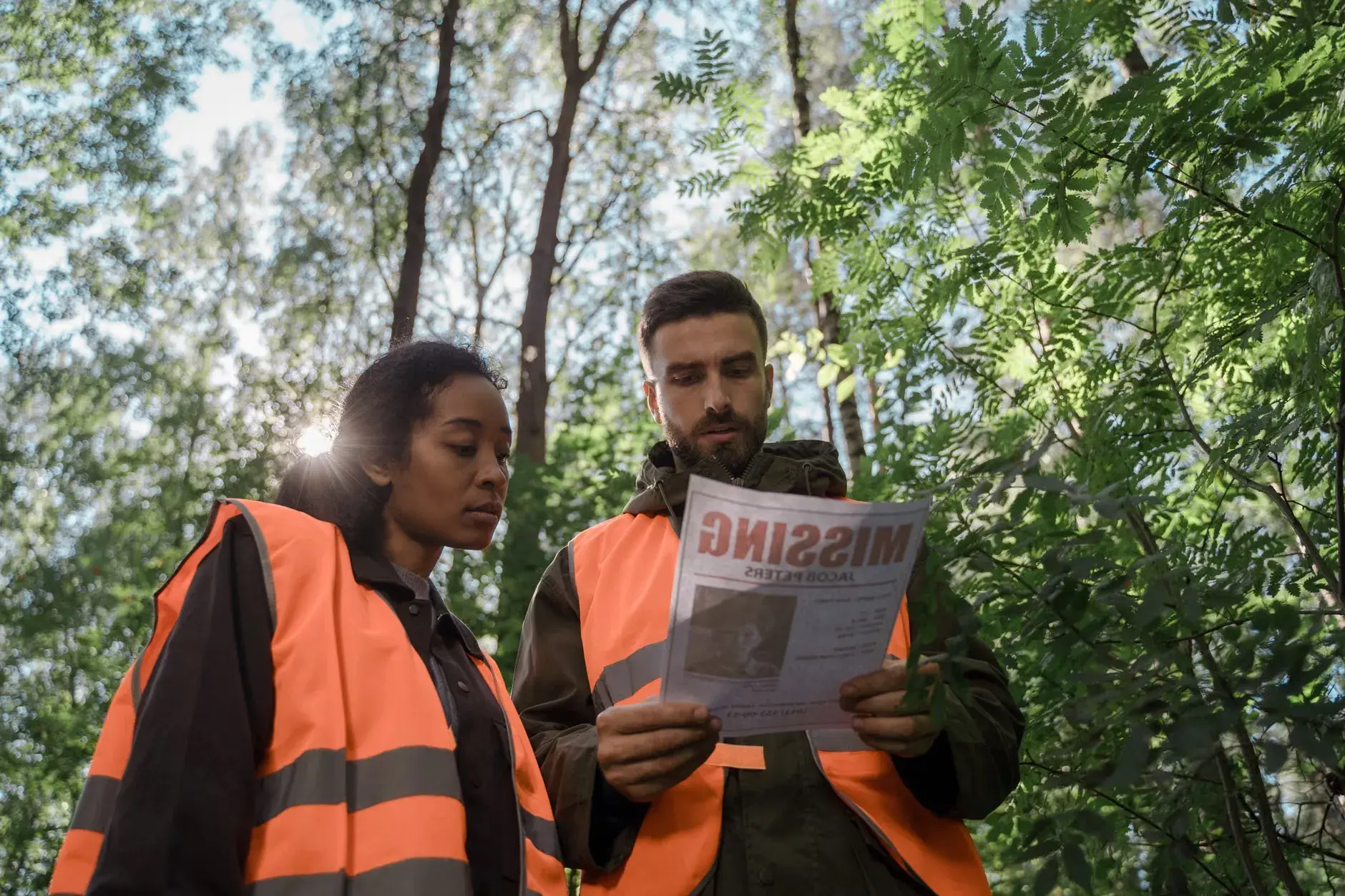 Et team iført sikkerhedsveste undersøger en savnet persons flyer i en skov. Scenen viser en alvorlig og fokuseret eftersøgning.