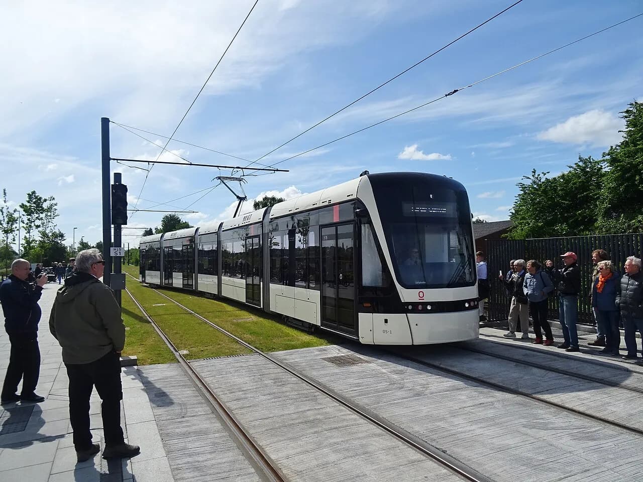 Det første tog på Odense Letbane ankommer til Hjallese Station i Odense, Danmark. Billedet markerer en vigtig begivenhed i byens offentlige transport.