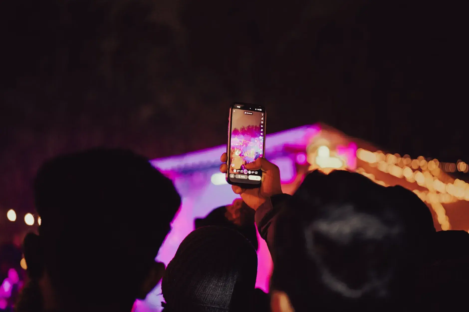 Publikum fotograferer en koncert i gang med smartphones under kraftige scenelys. Billedet indfanger den energiske stemning fra en live-aften.
