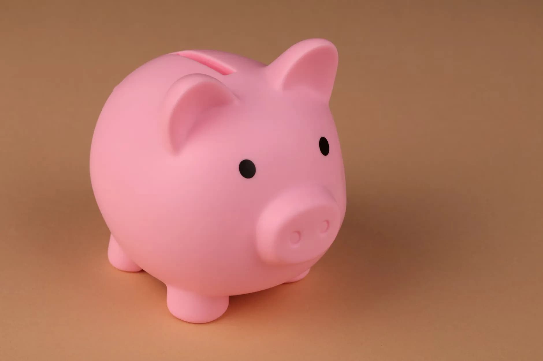 En rosa sparegris på en enkel brun baggrund, symboliserer spareøkonomi og budgettering. Billedet repræsenterer en simpel og effektiv måde at spare penge på.