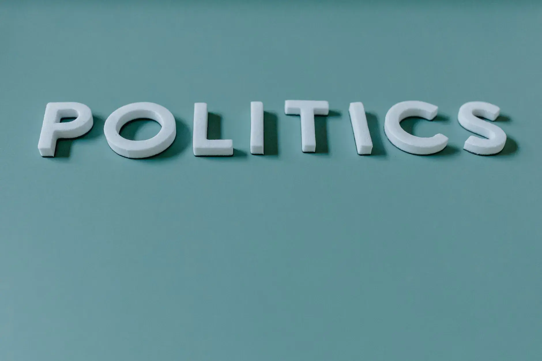 Tæt op på ordet 'Politik' mod en tealgrøn baggrund, der fremhæver politiske temaer.