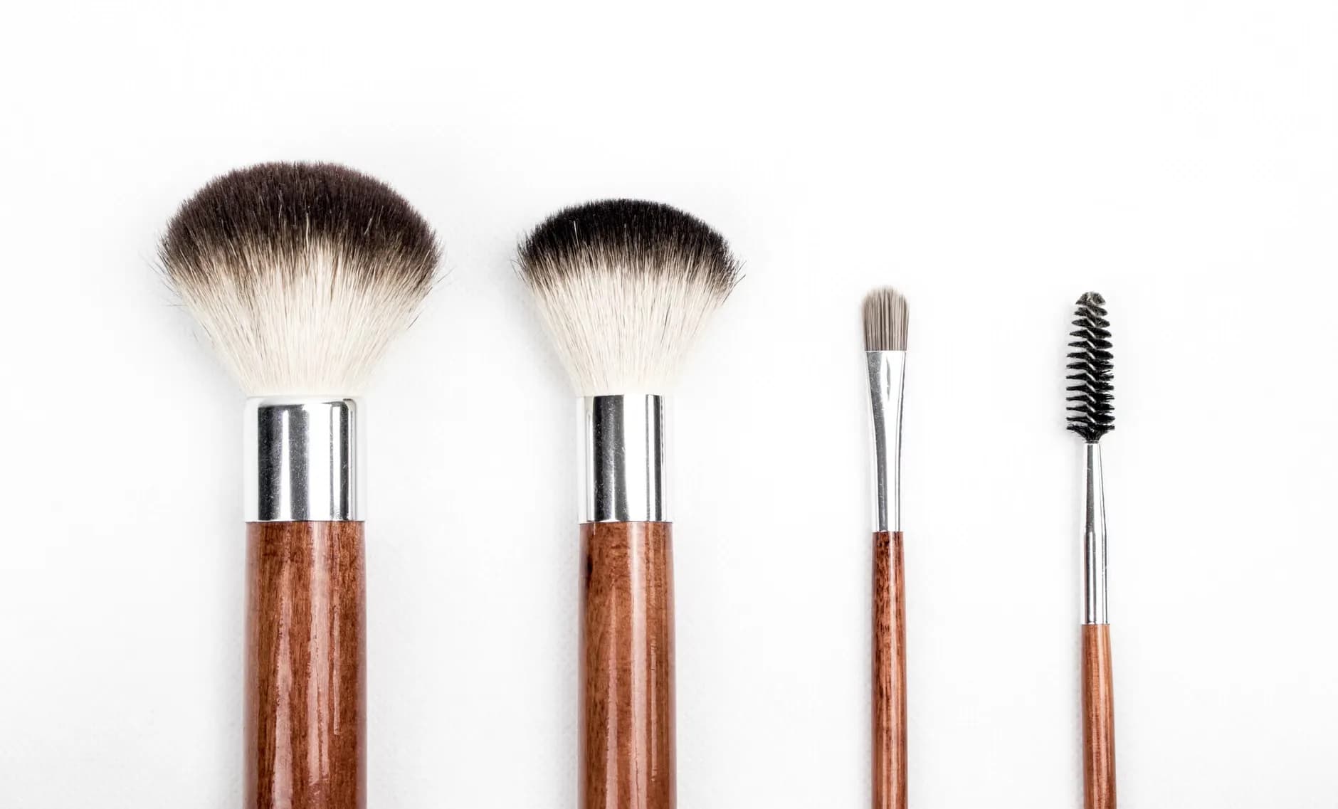 Stylish flat lay af fire træ makeup-børster placeret på en ren hvid baggrund.