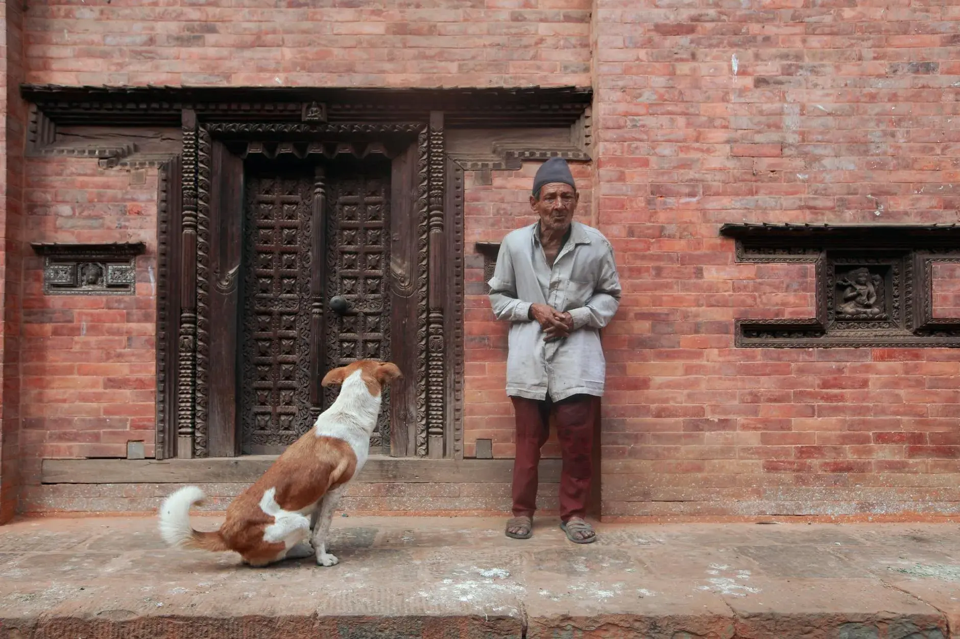 A serene scene featuring an elderly man and his dog standing near an intricately carved brick wall.