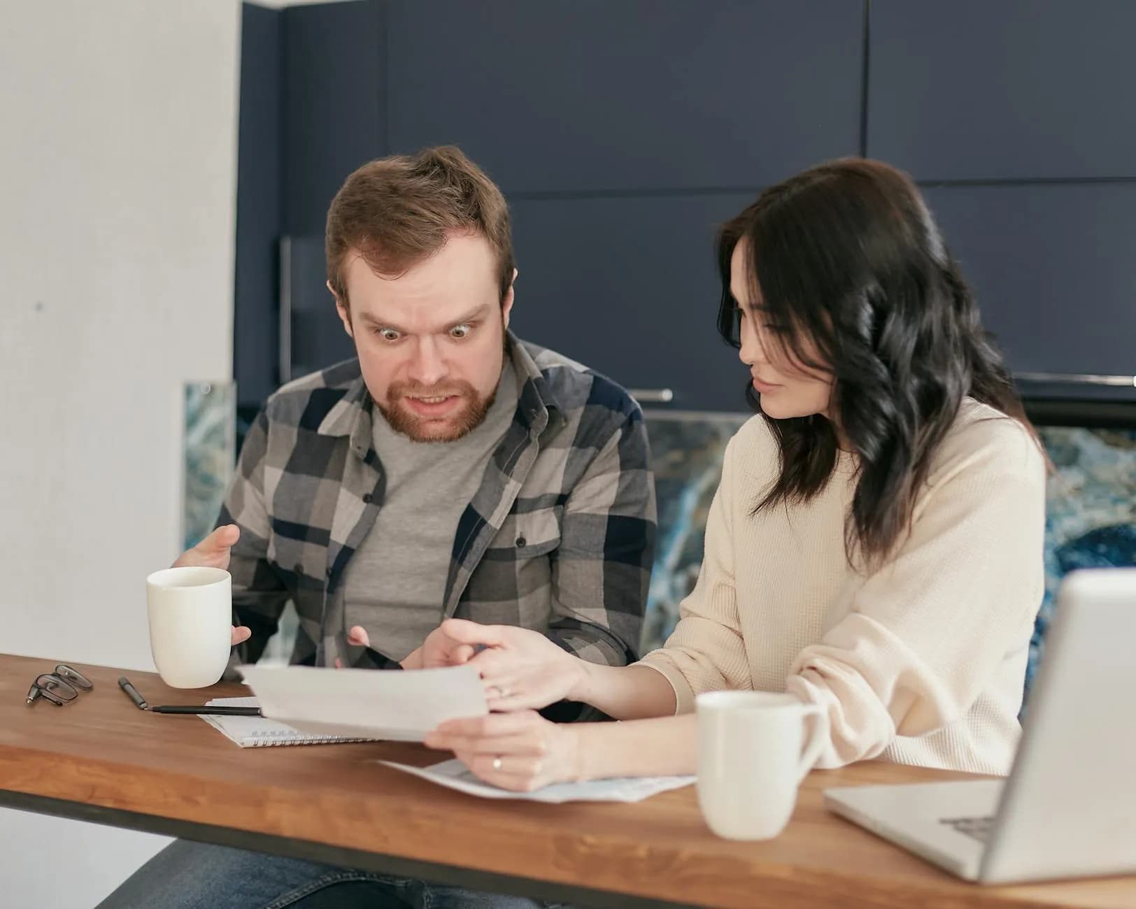 A couple stands at a wooden desk, stunned as they review important documents together indoors.