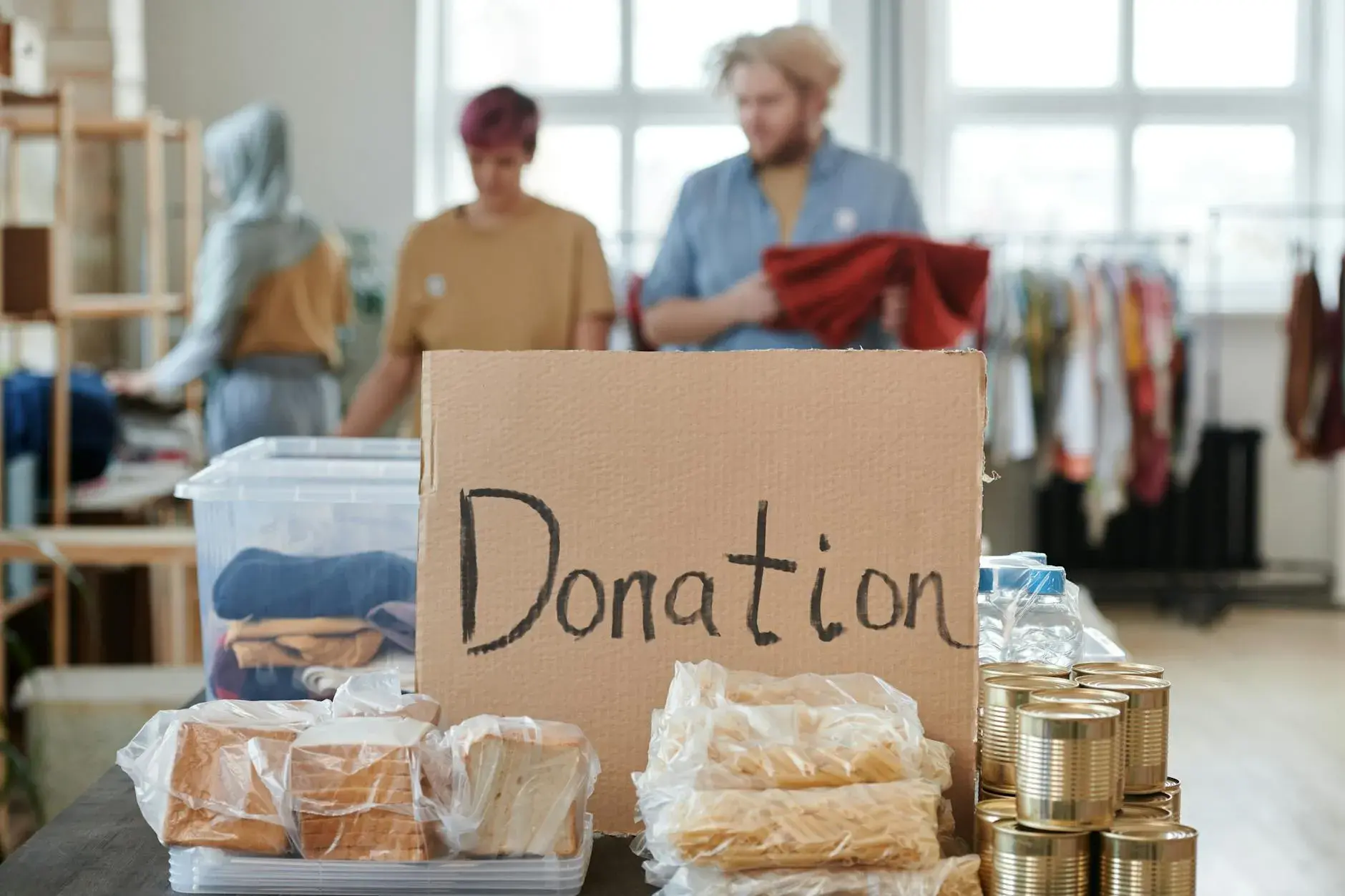 Frivillige sorterer tøj og madvarer i et donationscenter. Et skilt i pap med teksten “Donation” markerer indsamlingen.