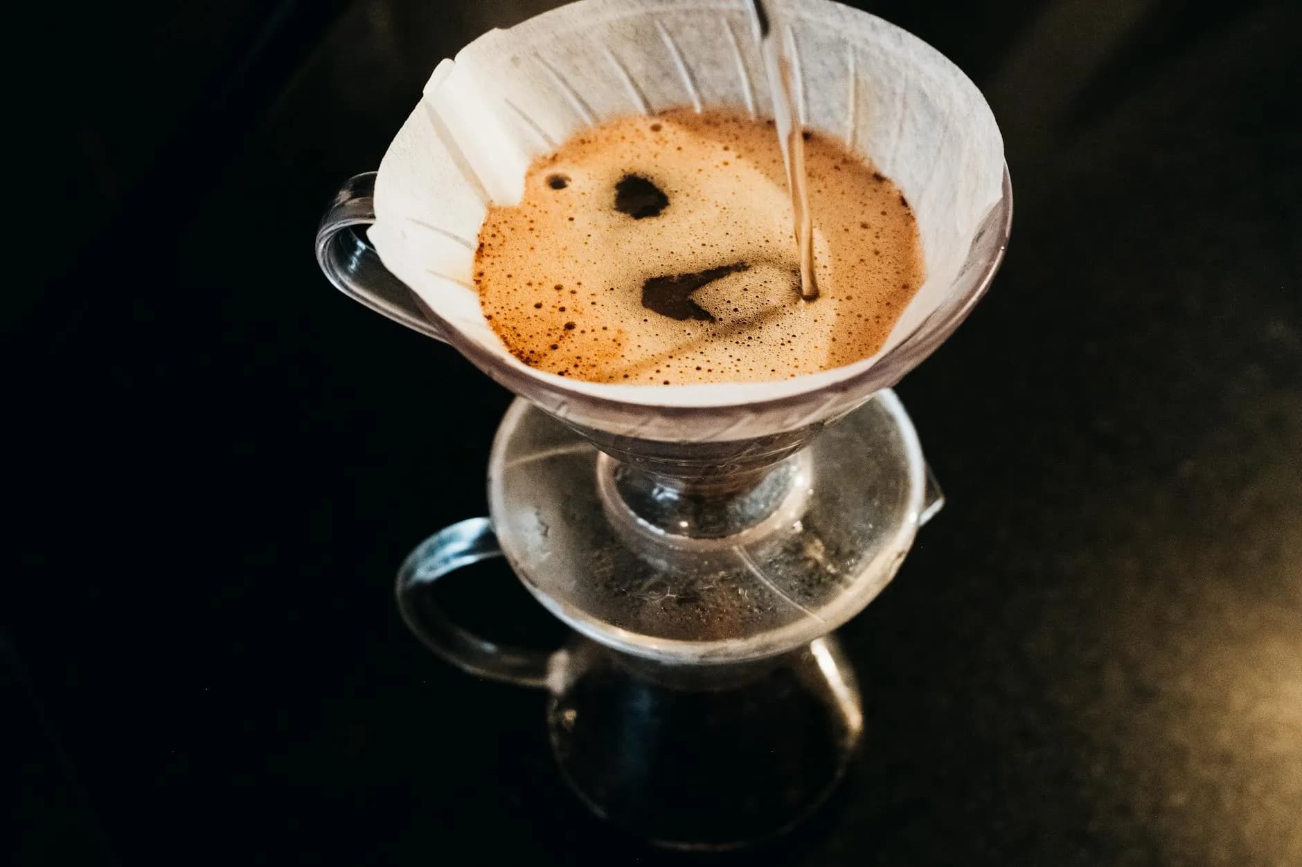 Set ovenfra af en pour-over kaffebrygningsproces med en filterdripper. Fokus er på den kontrollerede hældning og brygningens detaljer.