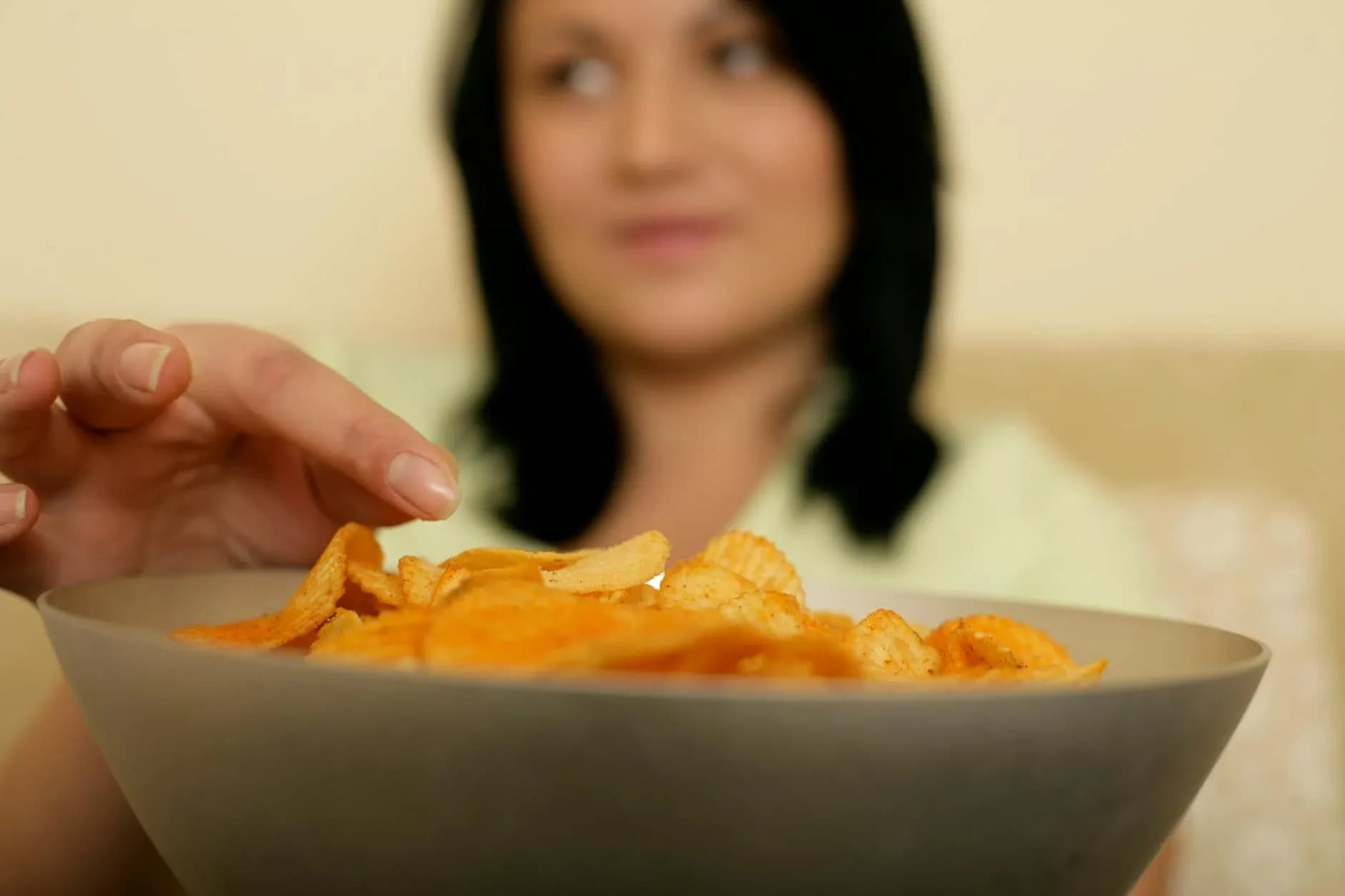 A candid moment capturing a woman's indulgent reach for a bowl of crispy potato chips.