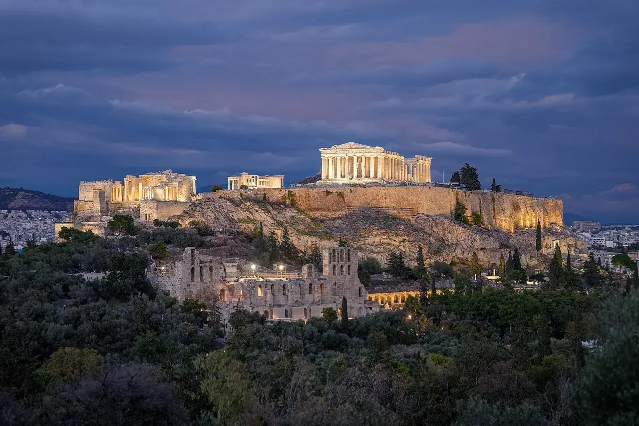 Akropolis oplyst i nattemørket i Athen. Billedet fanger stemningen og de dramatiske lysforhold ved monumentet.