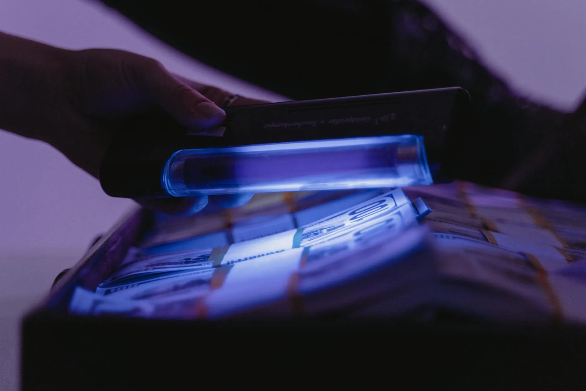 Nærbillede af banknoter under UV-lys for at kontrollere ægthed og afsløre eventuelle forfalskninger. Et visuelt eksempel på anti-fraud og sikkerhedskontrol.