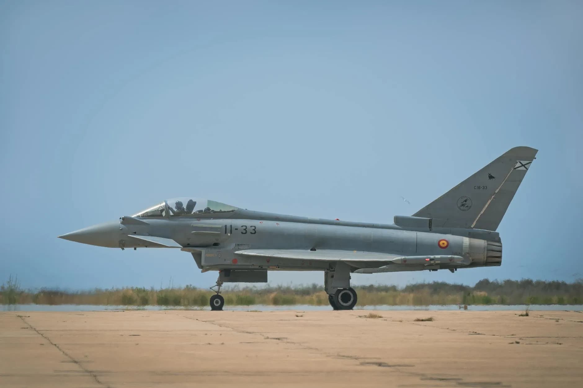 En Eurofighter Typhoon står parkeret på en landingsbane i dagslys. Billedet fanger et moderne militærfly i et åbent, operationelt miljø.