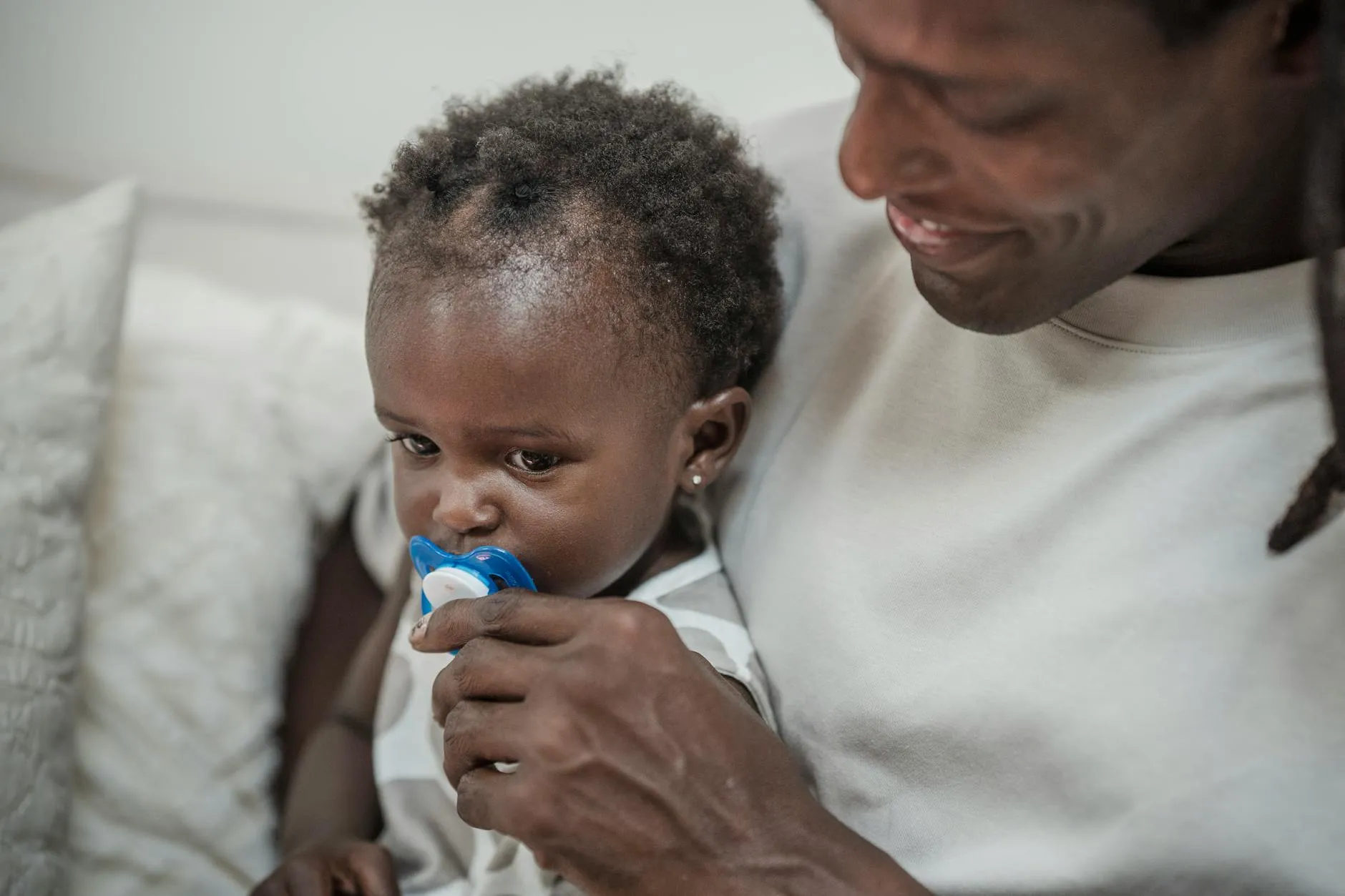 En far beroliger sin baby med en sut i sofaen og skaber et varmt, nært familiebillede. Stemningen er rolig og kærlig i et hjemligt miljø.