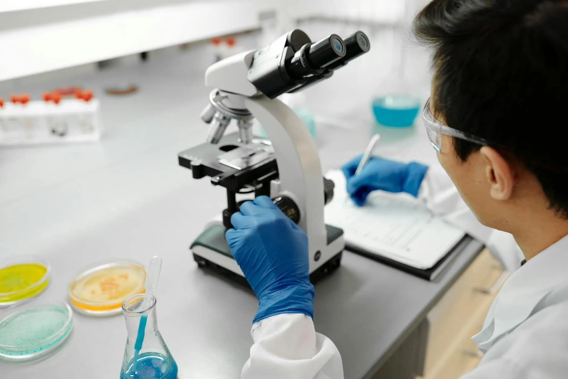 En forsker arbejder med et mikroskop i et moderne laboratorium for at analysere prøver. Billedet understreger præcision og videnskabeligt arbejde.
