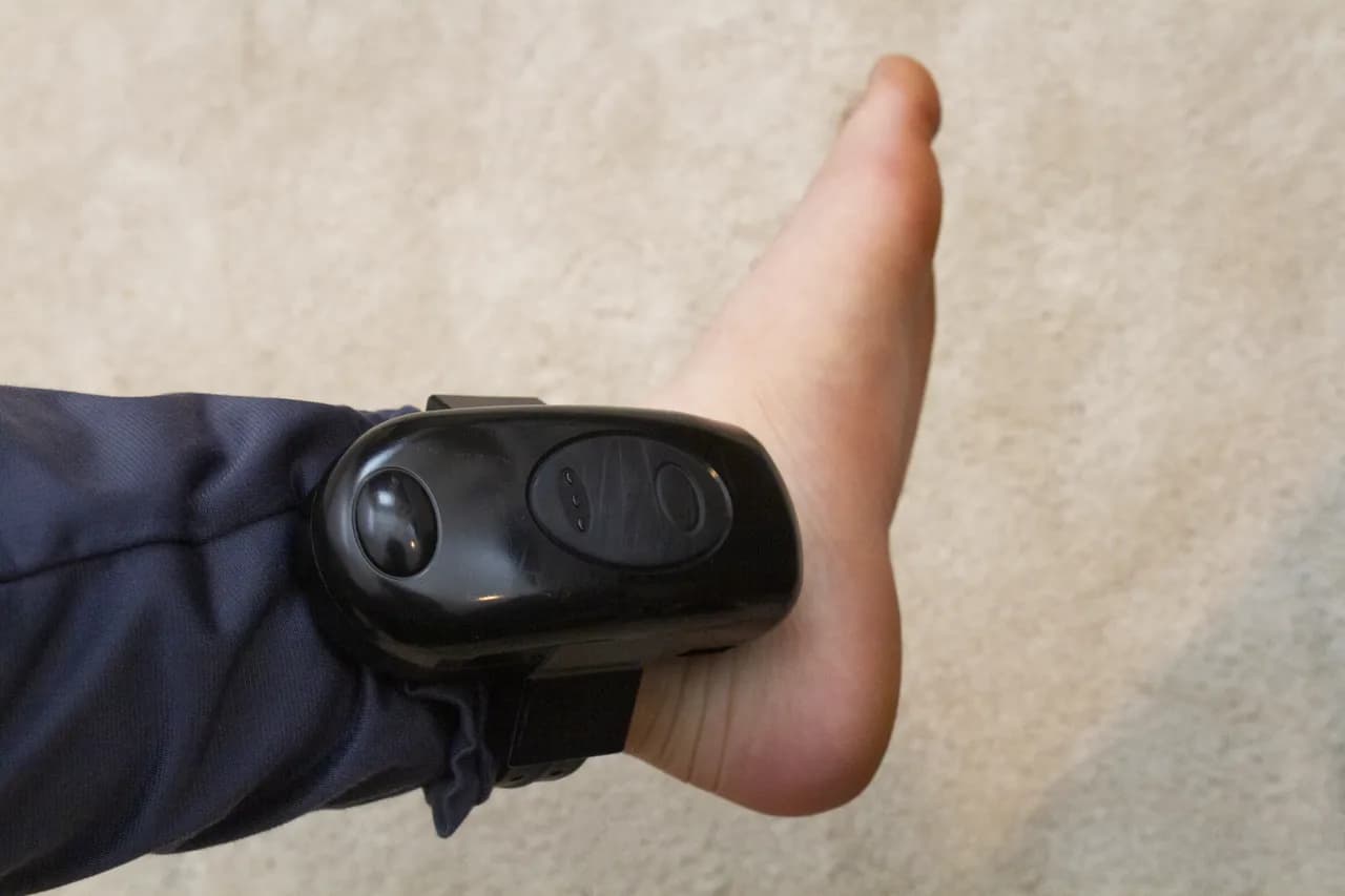 Et elektronisk ankelarmbånd (GPS tracking device) fastgjort til en person under husarrest. Billedet illustrerer overvågning og restriktioner.
