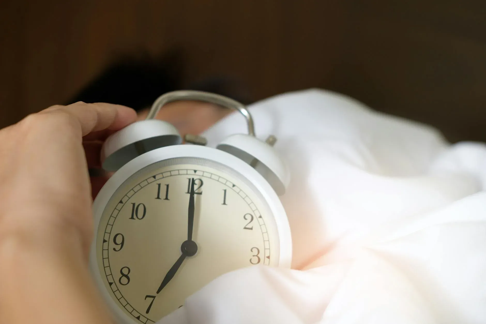 En hånd rækker ud efter et ringende vækkeur i et nærbillede. Motivet symboliserer at vågne om morgenen og komme i gang med dagen.