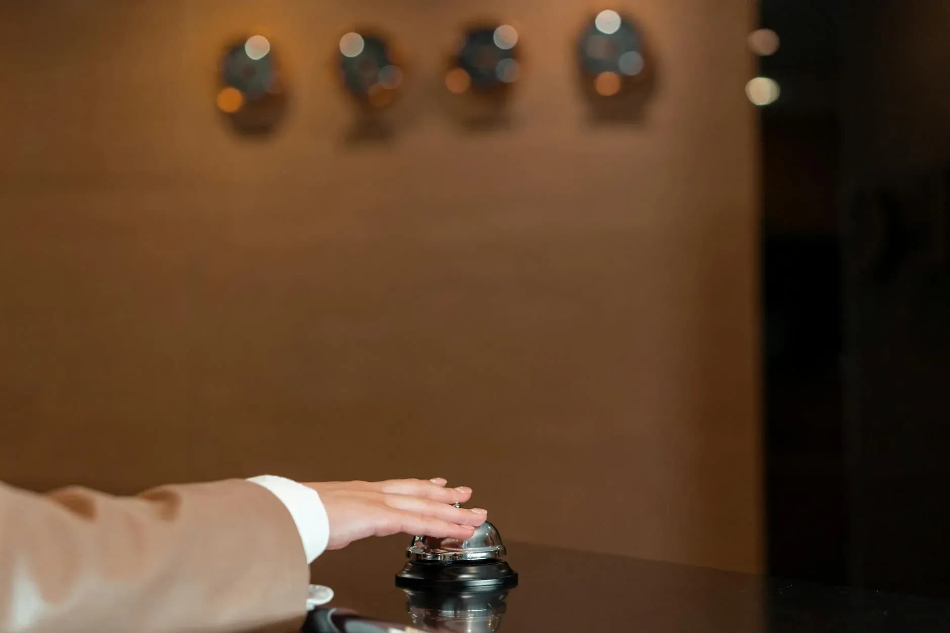 En hånd trykker på en klokke ved hotellets reception. Billedet symboliserer service, gæstfrihed og hurtig assistance.