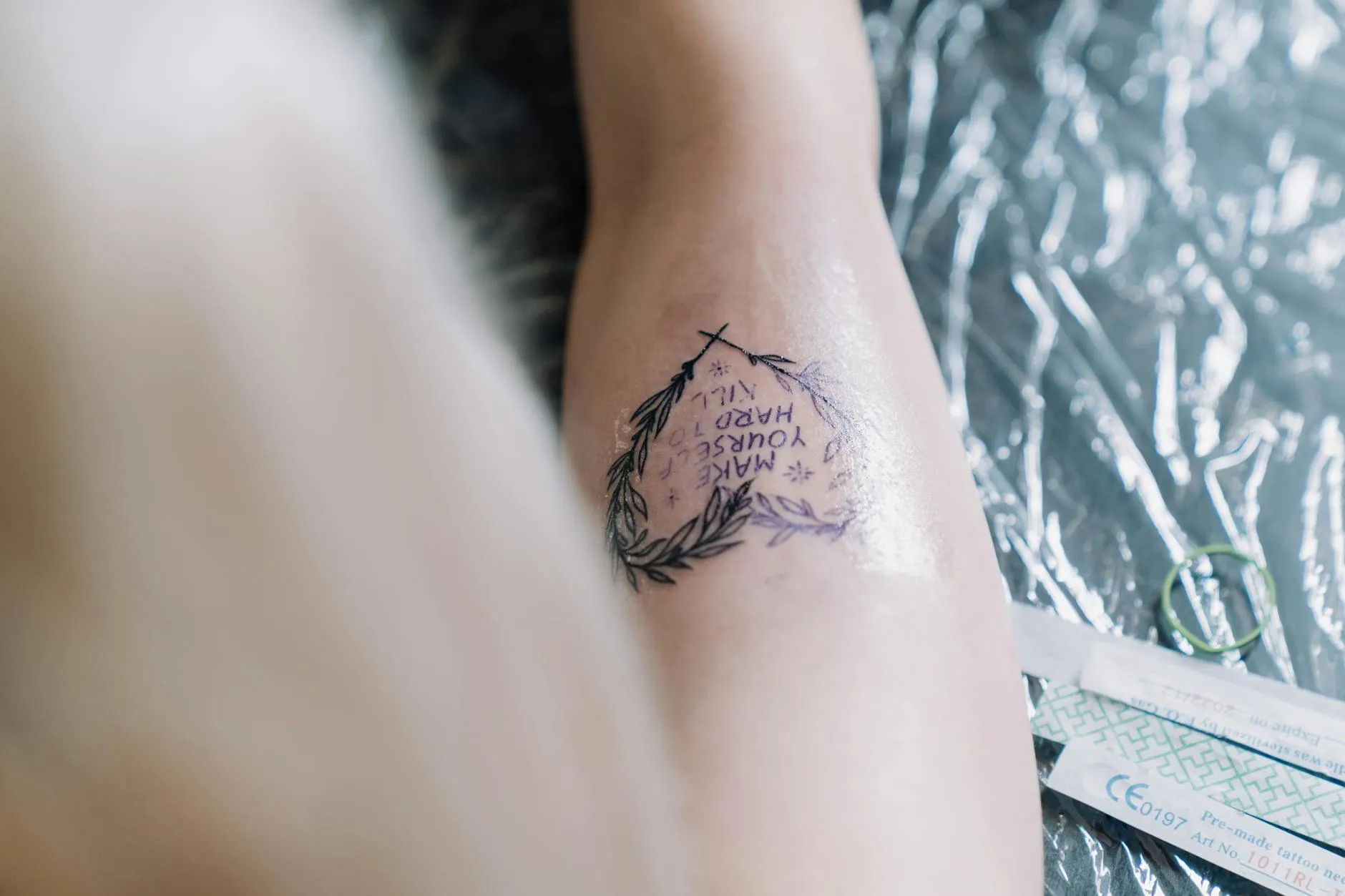 Close-up af en frisk tatovering med inspirerende tekst, omgivet af en laurbærkrans. Motivet ses tydeligt på huden.