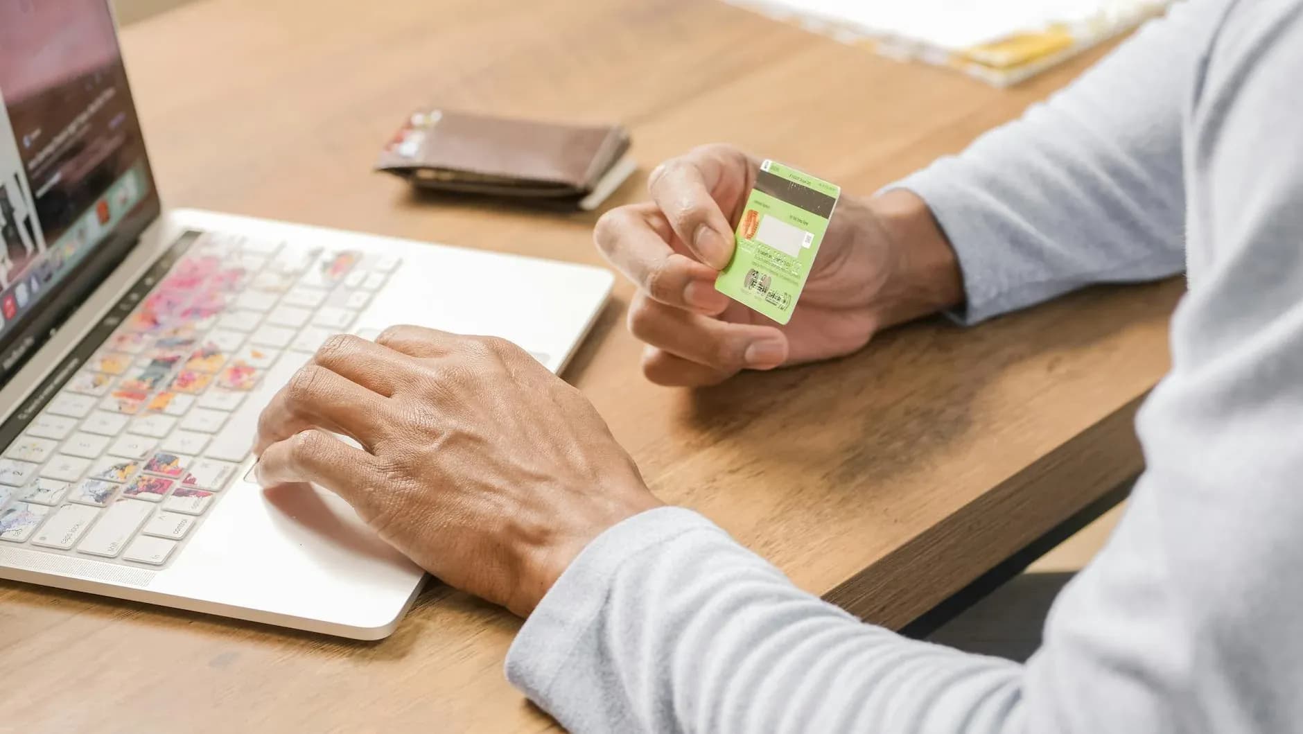 En person holder et kreditkort, mens der handles på en laptop. Billedet illustrerer en moderne online shoppingoplevelse.