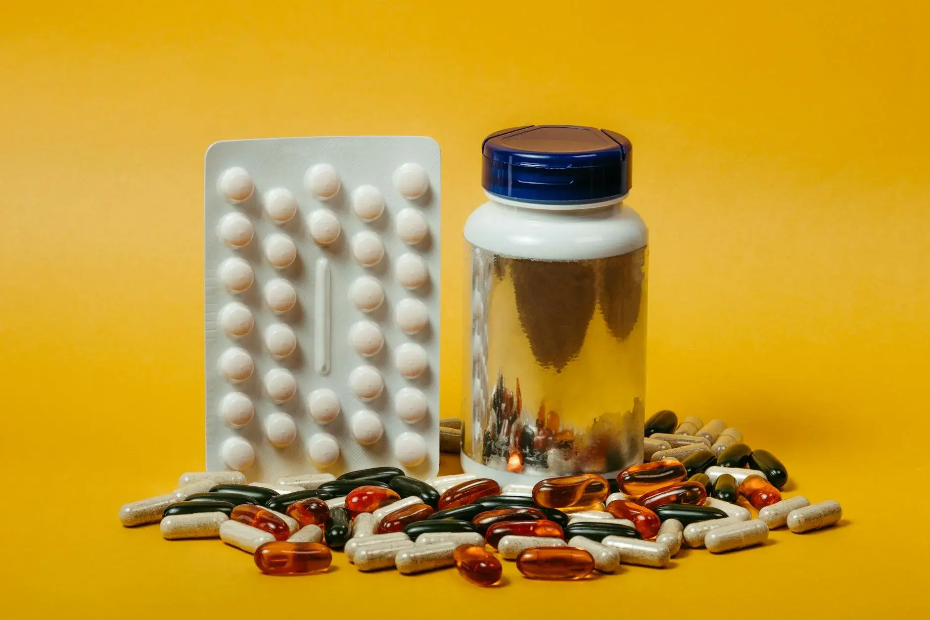 Et udvalg af piller og kapsler sammen med en flaske på en markant gul baggrund. Billedet egner sig til temaer om sundhed, medicin og velvære.