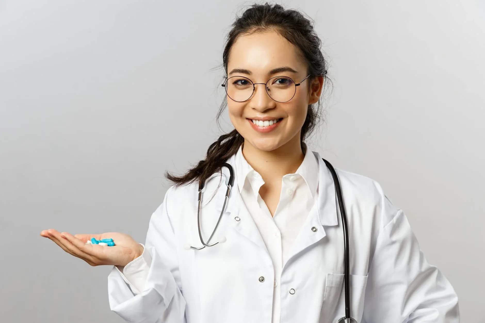 En kvindelig læge smiler og holder piller, mens hun formidler tryghed og behandling. Billedet understøtter temaer som sundhed, medicin og patientomsorg.
