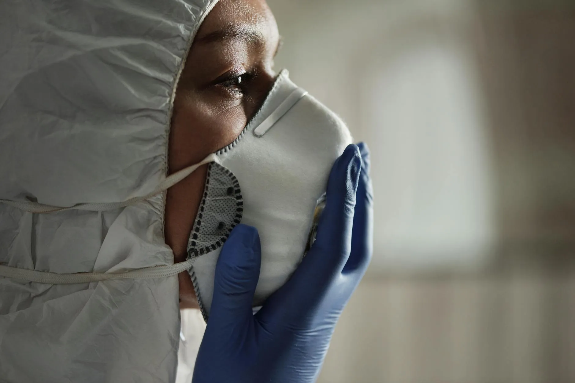 Et nærbillede af en sundhedsarbejder iført beskyttelsesdragt, maske og handsker. Billedet formidler fokus på sikkerhed og hygiejne i sundhedssektoren.