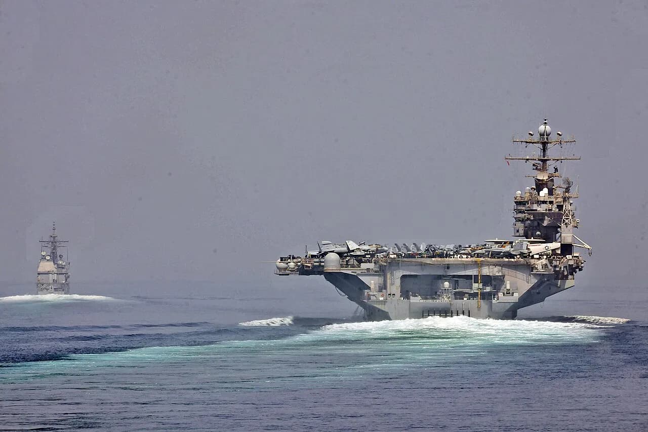 USS Cape St. George og hangarskibet USS Abraham Lincoln sejler gennem strædet ved Hormuz under maritime sikkerhedsoperationer. Billedet illustrerer skibenes passage i et af verdens mest strategiske farvande.