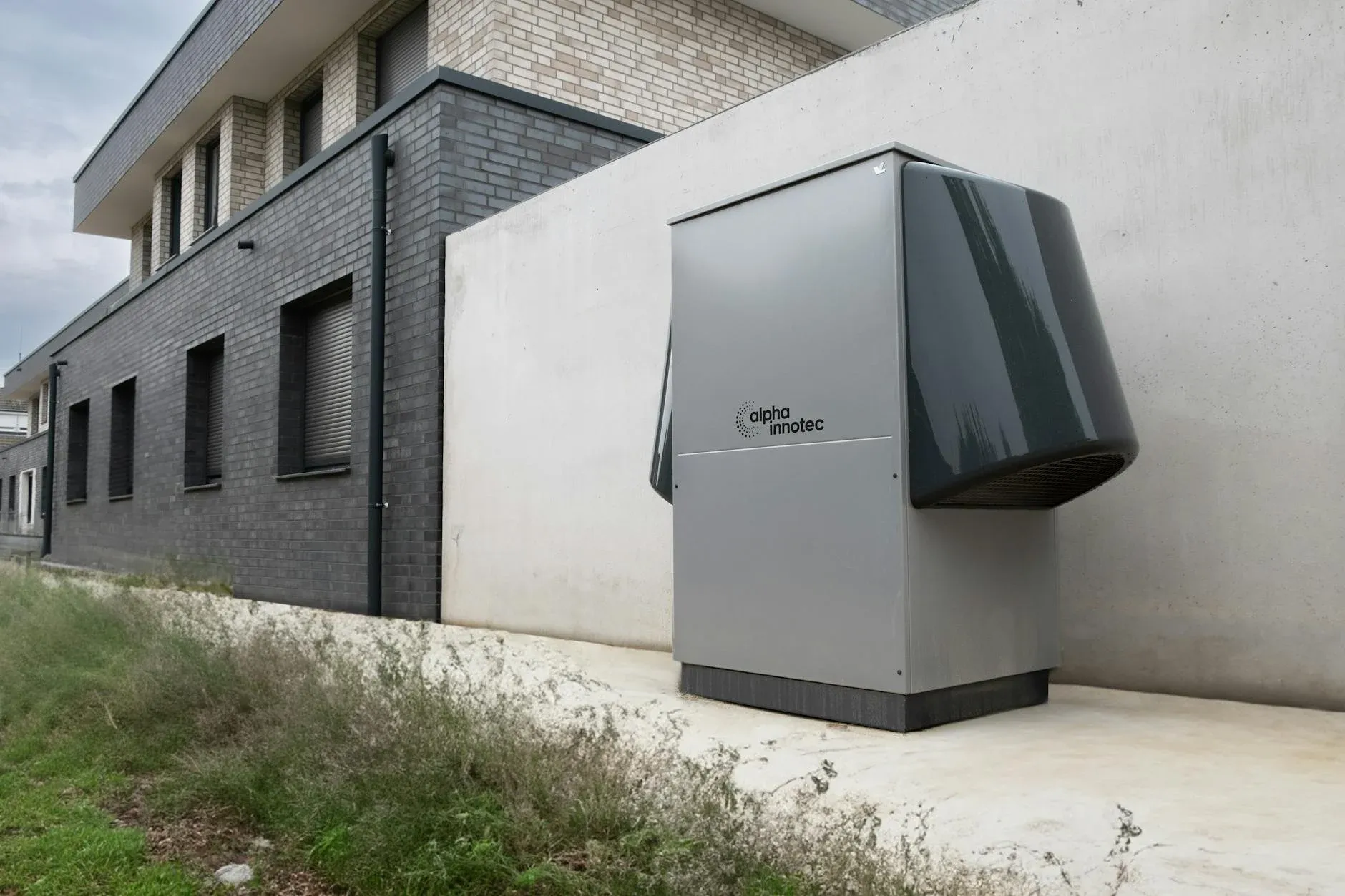 En innovativ varmepumpeenhed fra alpha innotec er installeret udendørs ved en moderne bygning. Billedet illustrerer effektiv opvarmning og energiløsninger i boligmiljøer.