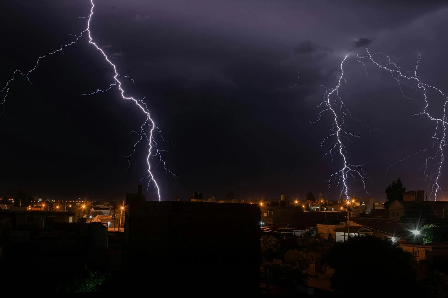 Et kraftigt lynnedslag oplyser en by i mørket under en natlig tordenstorm. Stemningen fremhæver naturens intensitet og dramatik.