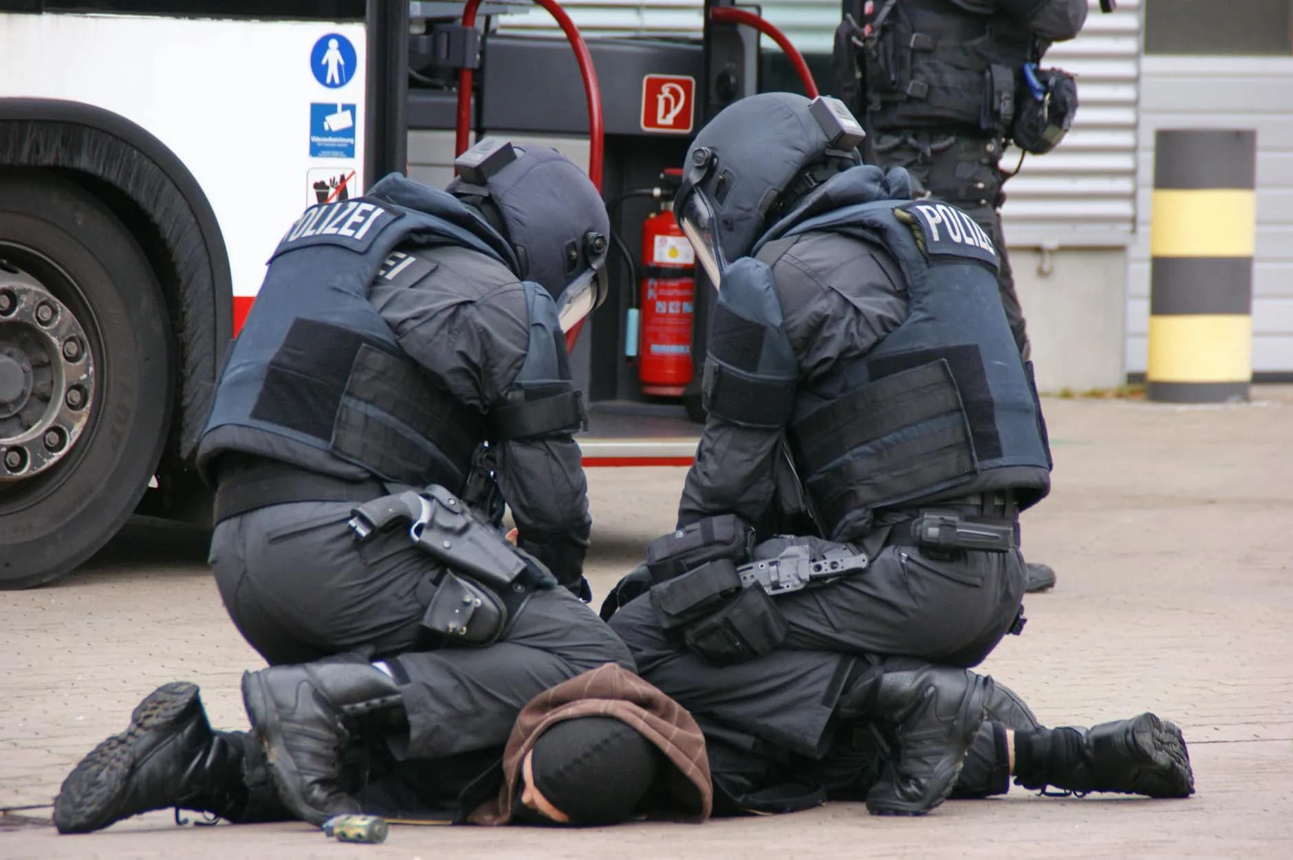 Tysk politi i fuldt udstyr tilbageholder en mistænkt i et byområde i Hamburg. Scenen er fotograferet i en dokumentarisk stil.