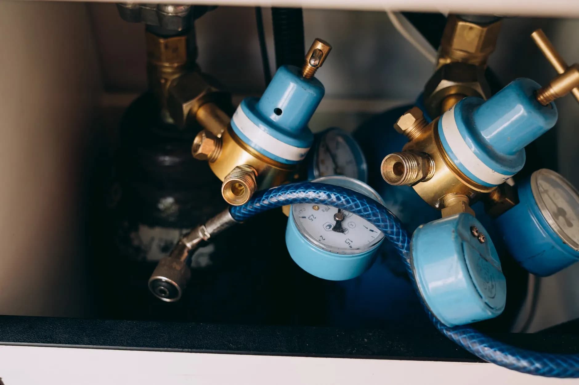 Et detaljeret billede af blå og messing gas trykregulatorer med måleinstrumenter og rør i et industrielt miljø. Billedet viser komplekse mekanismer og teknisk udstyr.