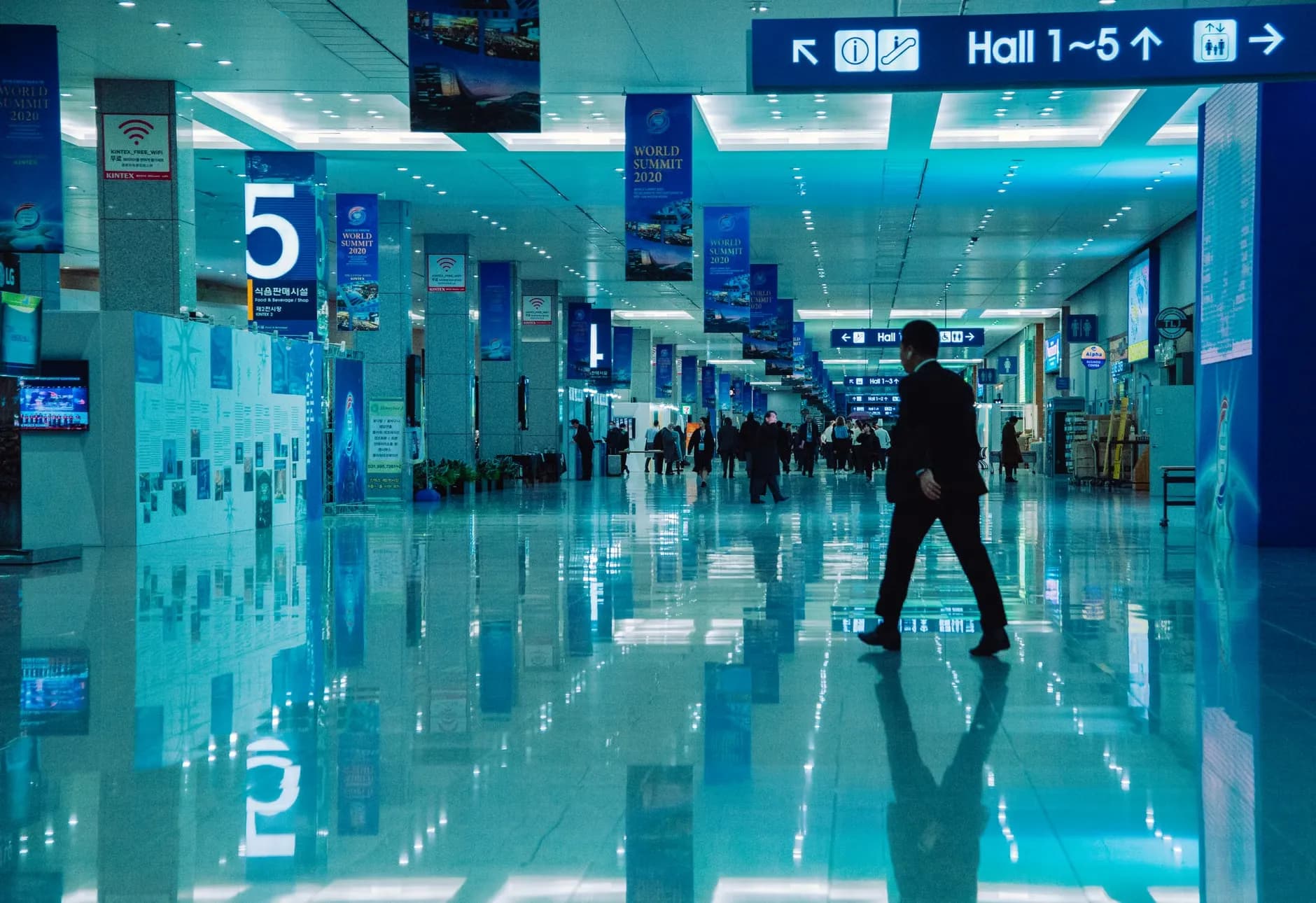 En indendørs optagelse af en travl konferencehal under World Summit 2020 med retningsskilte og reflekser.