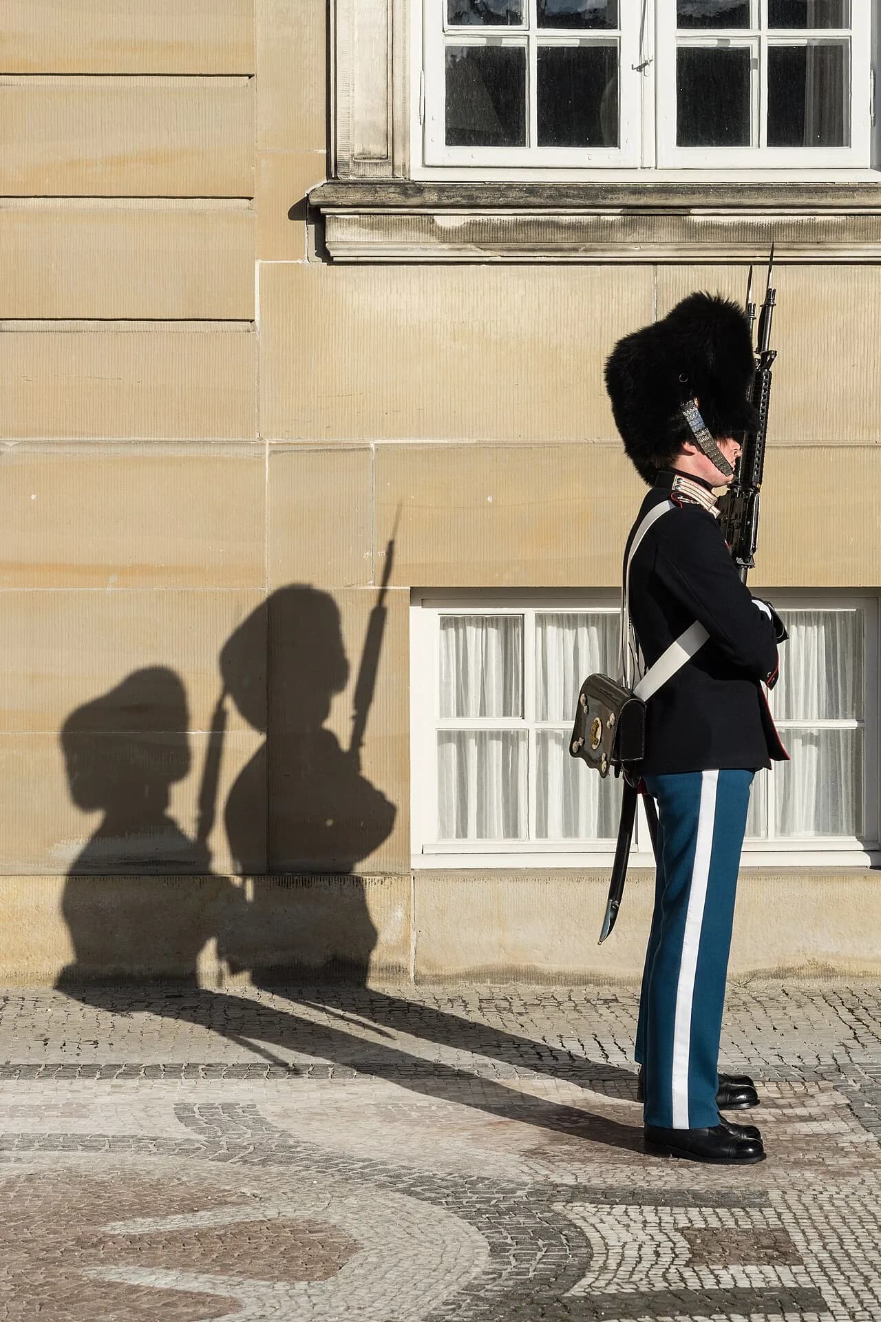 To medlemmer af Den Kongelige Livgarde står vagt ved Amalienborg Slot i København. Billedet fanger uniformerne og den ceremonielle stemning.