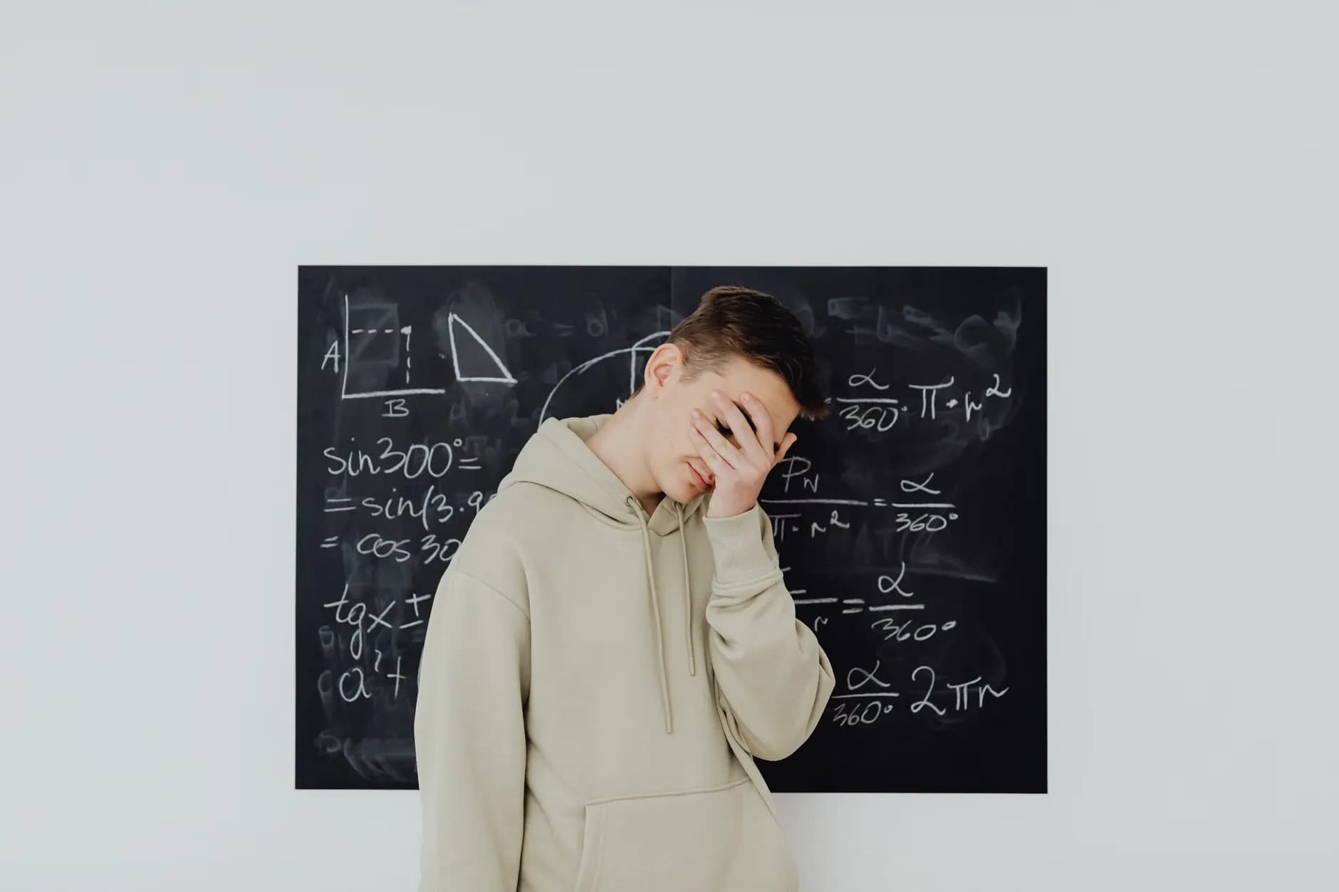 En teenager dækker ansigtet med frustration foran en tavle fyldt med matematikligninger, hvilket afspejler akademisk stress.
