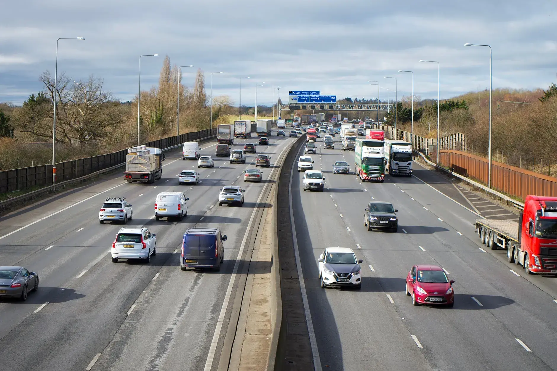 Billede af en travl motorvej i St Albans, UK, med mange biler og lastbiler under dagtid. Motorvejen er fyldt med trafik.