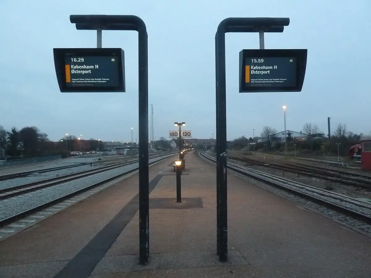 Railway platform with tracks and departure boards at dusk.