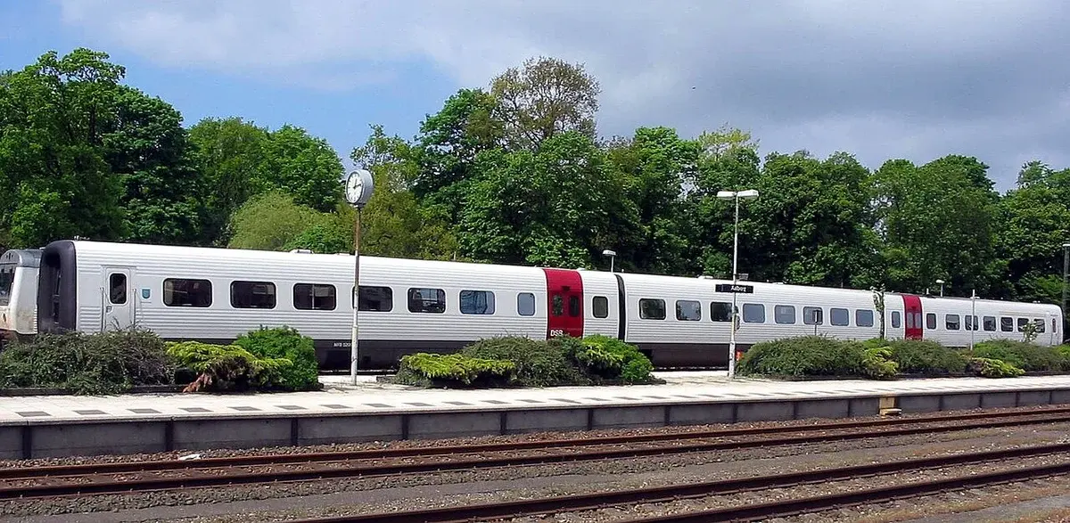 A DSB Intercity train stopped at a station platform with trees in the background.