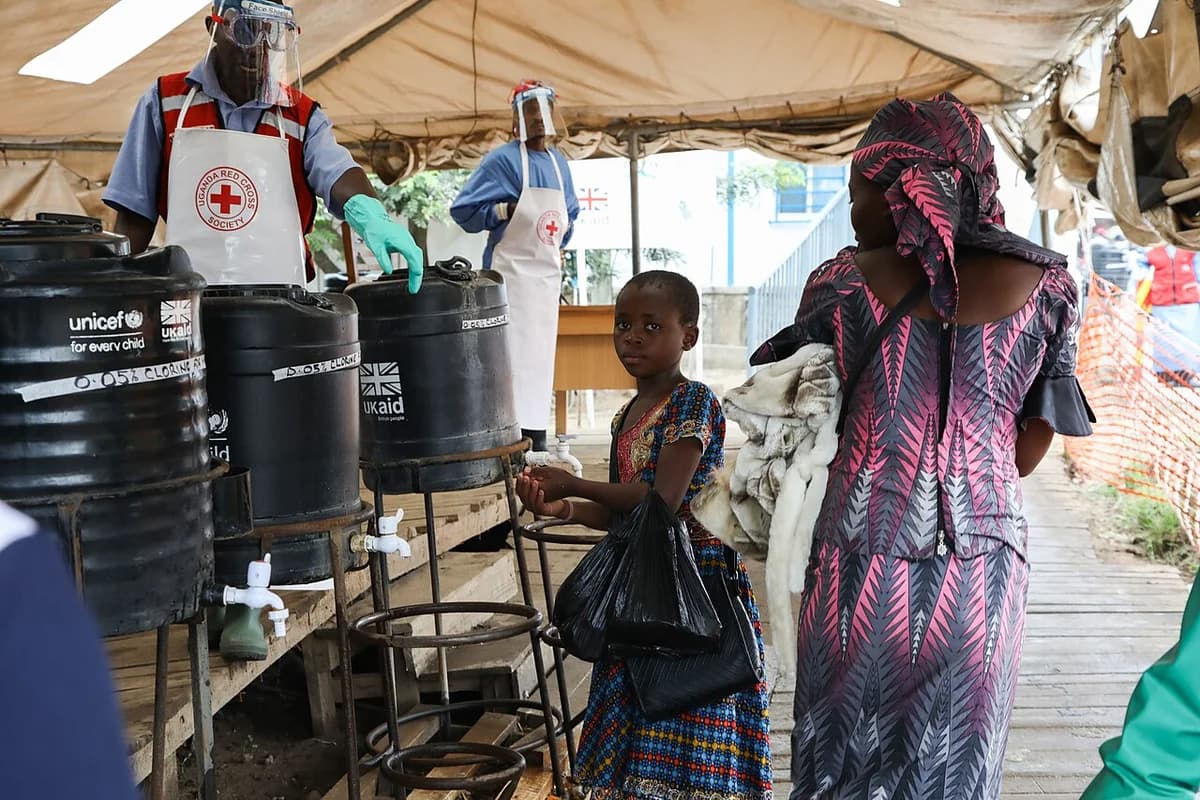 A girl washes her hands at an Ebola checkpoint while health workers supervise.