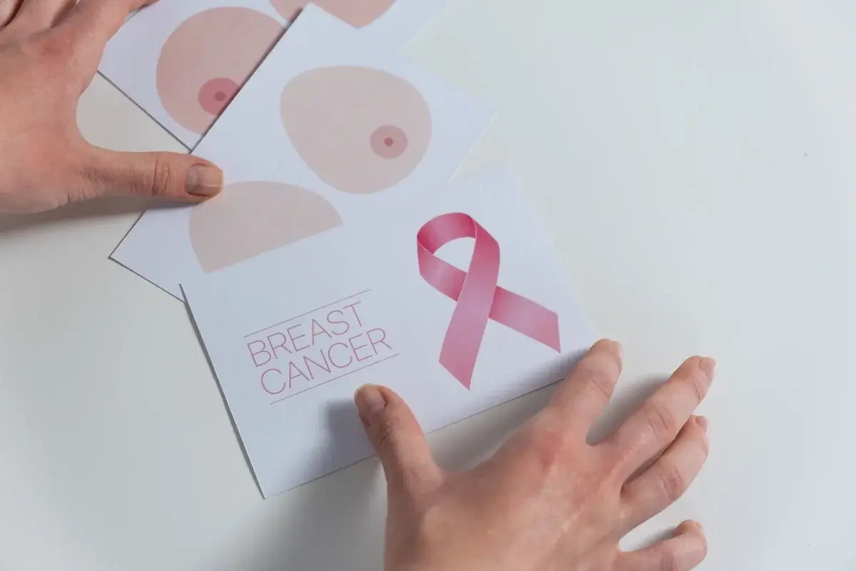 Hands arranging breast cancer awareness cards with a pink ribbon.
