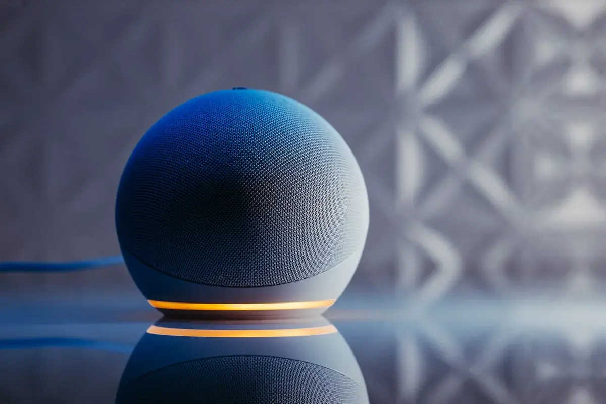 A spherical smart speaker with a glowing base on a reflective surface.