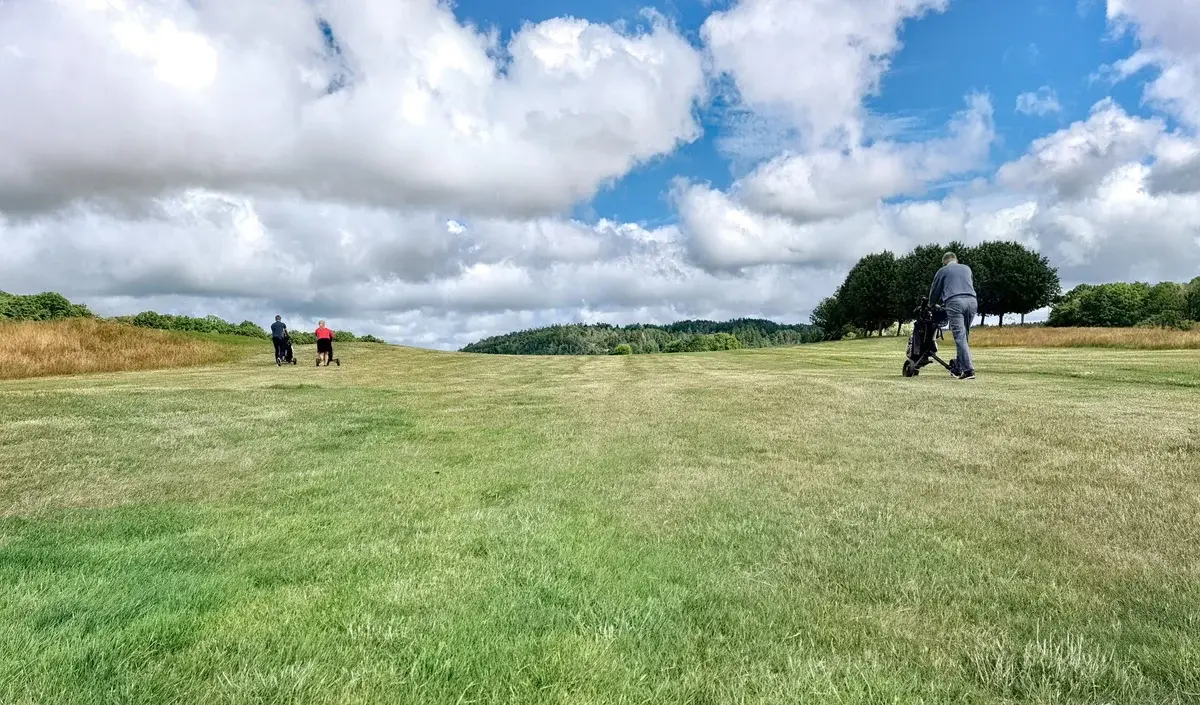 Golfers walking across a grassy golf course under cloudy skies.