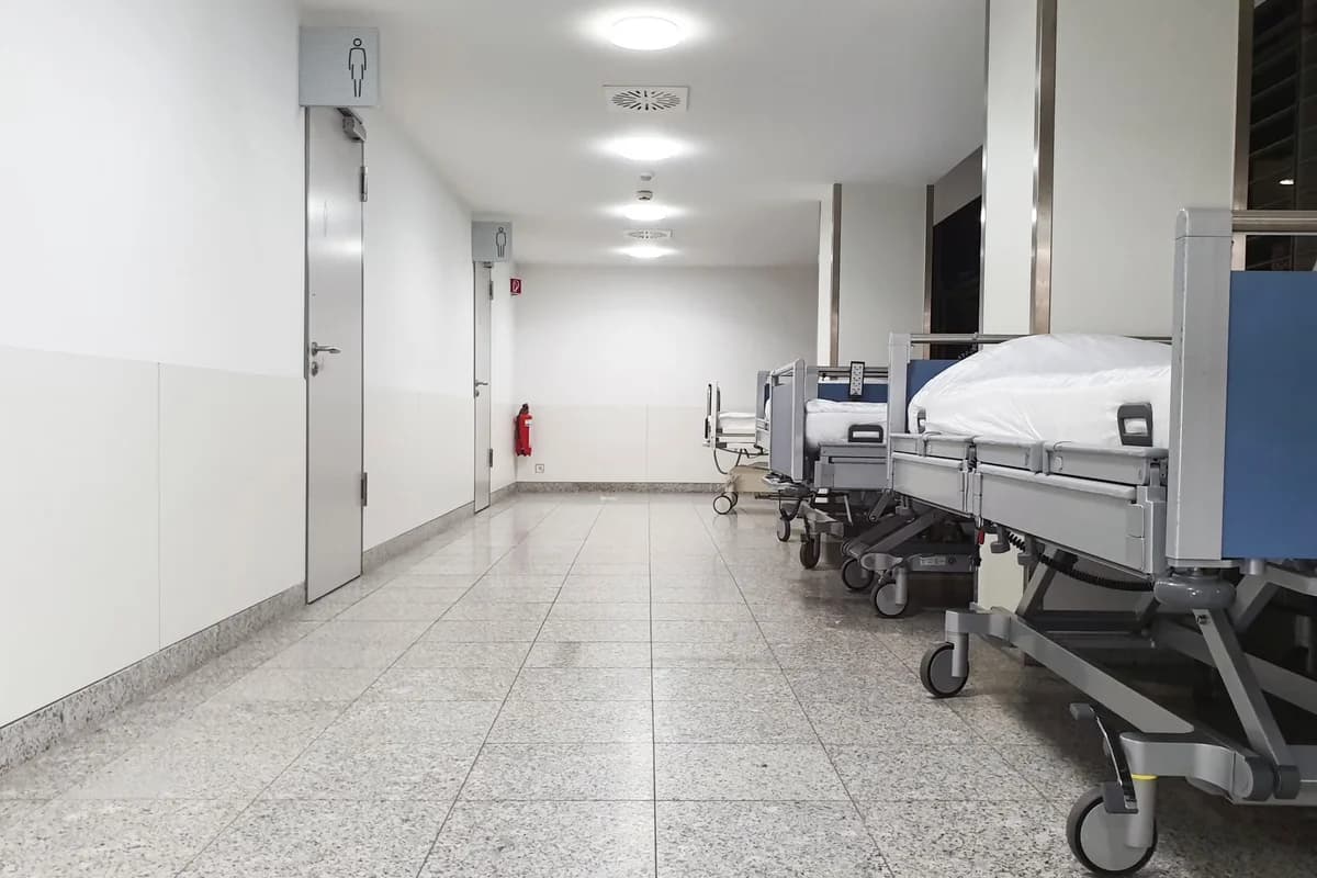 Empty hospital corridor with several beds lined up on the right side.