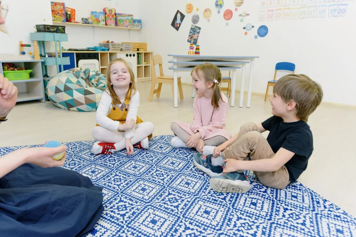 Three young children sitting and playing on a classroom rug in a kindergarten room.