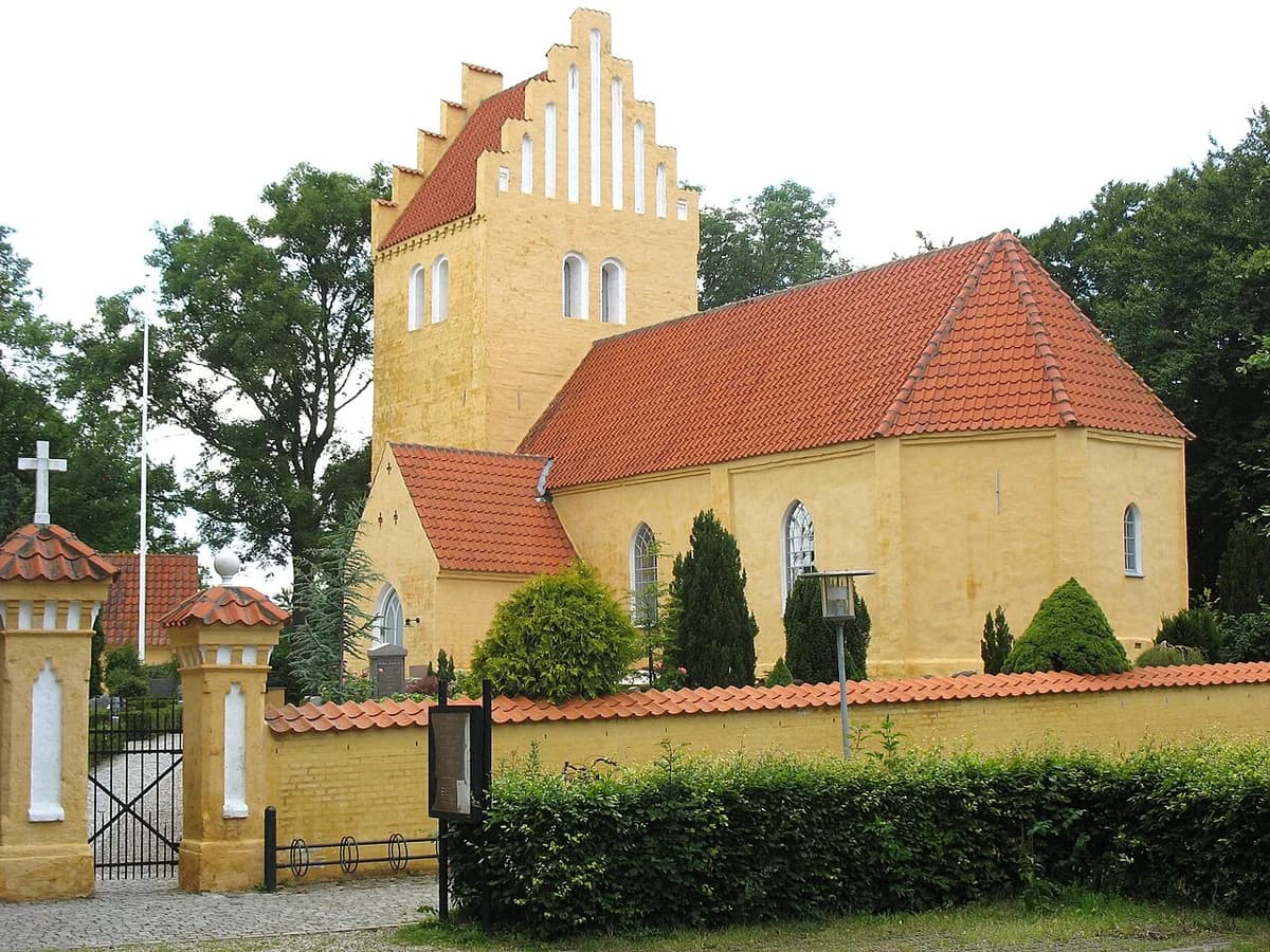 A yellow church with a red roof and stepped gable tower behind a wall and gate.