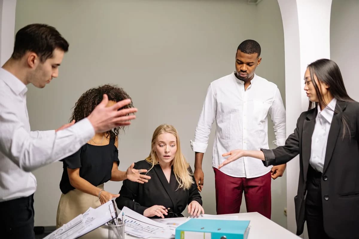 Diverse colleagues arguing or discussing intensely around a seated woman in an office.