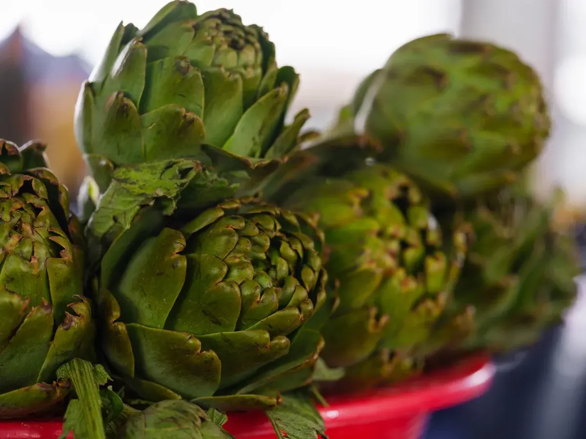 Close-up of fresh artichokes on a red tray at a market stall.