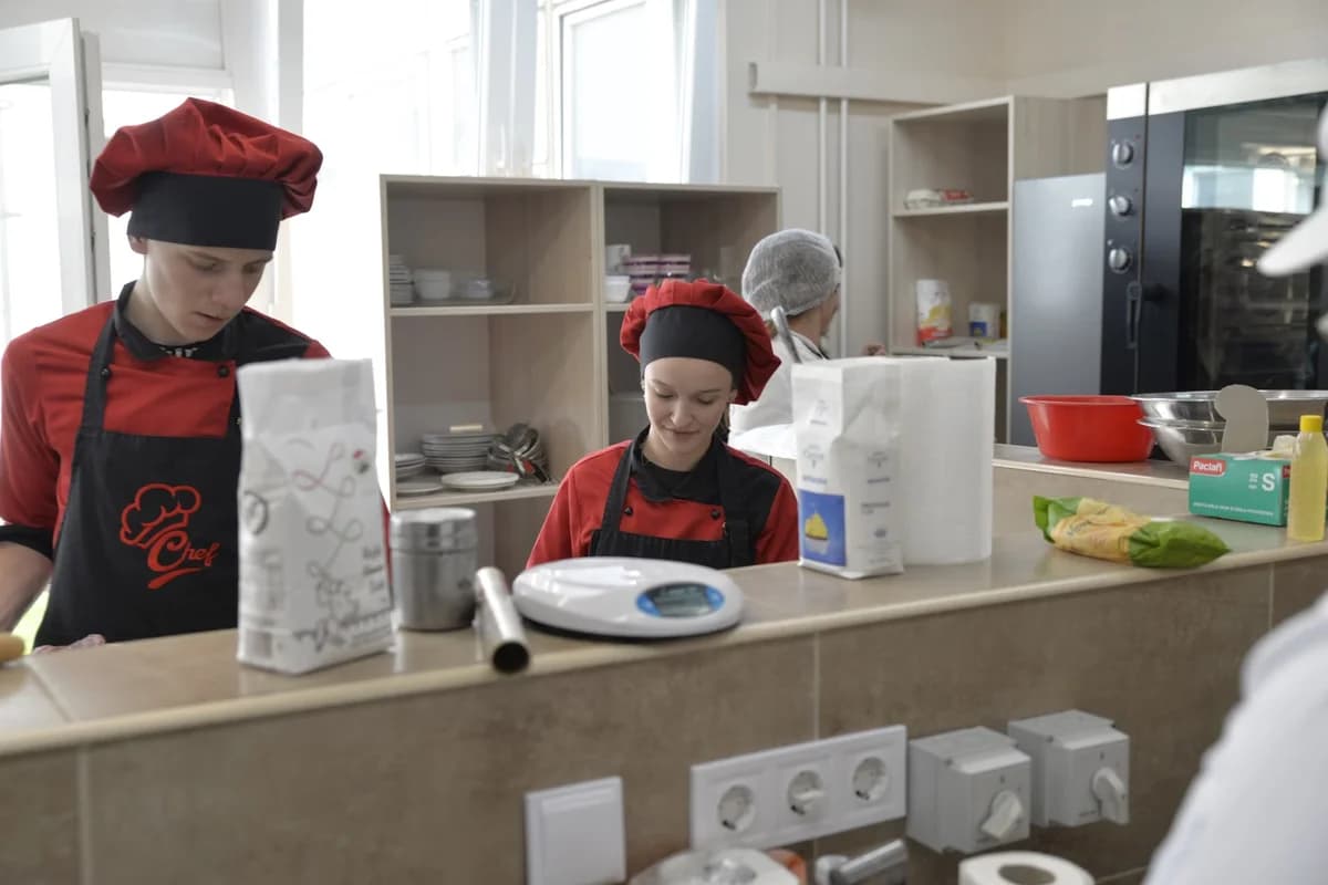 Culinary students in red chef uniforms working in a professional kitchen.