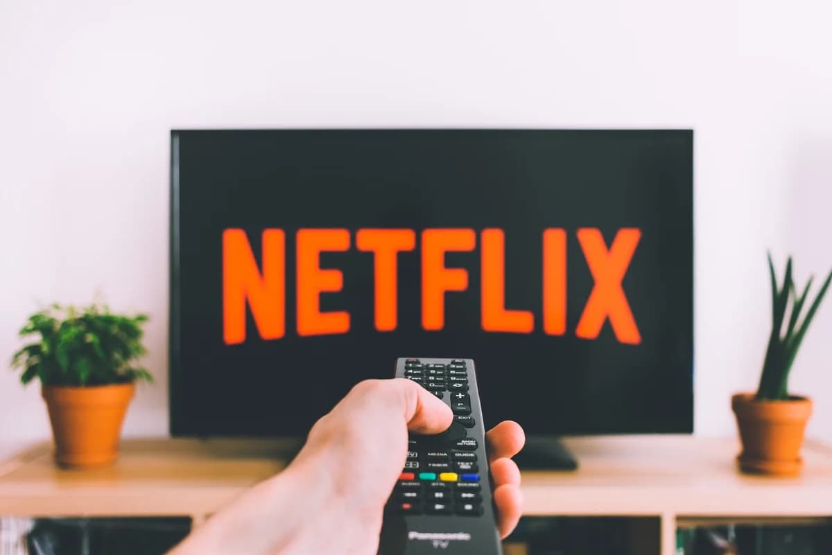A hand holding a remote pointed at a TV showing the Netflix logo.